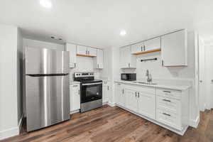 Downstairs kitchen featuring appliances with stainless steel finishes, white cabinetry, dark wood-style flooring, and recessed lighting
