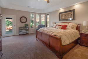 Carpeted bedroom with multiple windows, access to outside, a ceiling fan, and a raised ceiling