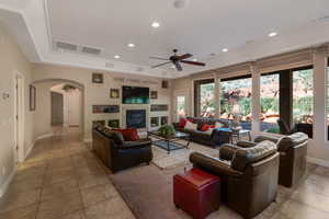 Living area with a tray ceiling, a ceiling fan, light tile patterned flooring, recessed lighting, and a glass covered fireplace