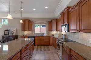 Kitchen featuring black appliances, dark stone countertops, decorative backsplash, brown cabinetry, and recessed lighting