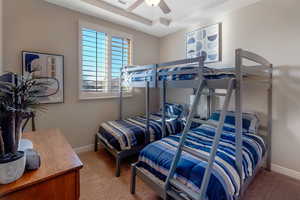 Bedroom featuring a raised ceiling, light carpet, and a ceiling fan