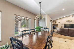 Dining room featuring vaulted ceiling, recessed lighting, light tile patterned floors, a chandelier, and a stone fireplace