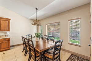 Dining space featuring light tile patterned floors, vaulted ceiling, and a chandelier