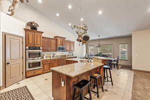 Kitchen featuring brown cabinetry, a breakfast bar, a spacious island, a chandelier, and stainless steel appliances