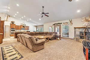 Living room with light colored carpet, recessed lighting, a stone fireplace, high vaulted ceiling, and a ceiling fan