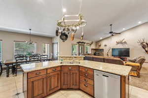 Kitchen with brown cabinets, dishwasher, a chandelier, a center island with sink, and light tile patterned floors