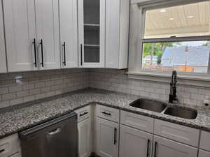 Kitchen with dishwasher, dark stone counters, white cabinetry, and tasteful backsplash