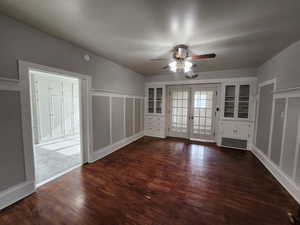 Empty room featuring dark wood finished floors, ceiling fan, french doors, and a decorative wall