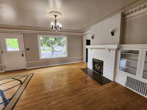 Unfurnished living room featuring hardwood / wood-style floors, a chandelier, a brick fireplace, and ornamental molding