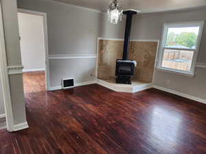 Unfurnished living room with a wood stove, dark wood finished floors, and ornamental molding