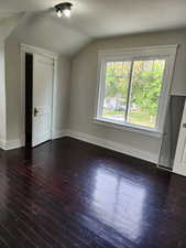 Additional living space with dark wood-style floors and vaulted ceiling
