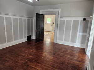 Unfurnished room featuring a decorative wall, dark wood finished floors, a wainscoted wall, and ceiling fan