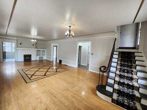 Unfurnished living room with hardwood / wood-style flooring, a chandelier, a brick fireplace, crown molding, and stairs