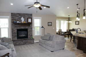Living area with a stone fireplace, recessed lighting, ceiling fan, and stone tile flooring