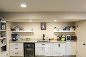 Indoor wet bar with open shelves, white cabinets, wine cooler, light stone counters, and recessed lighting