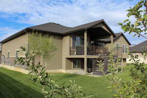 Rear view of property with a lawn, stairs, stucco siding, a patio, and a balcony