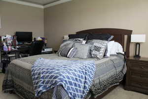 Bedroom with light colored carpet, a desk, and ornamental molding