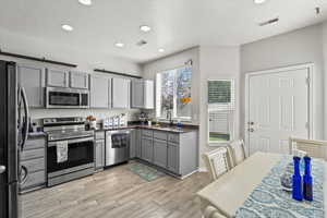 Kitchen featuring gray cabinets, stainless steel appliances, recessed lighting, light wood finished floors, and dark stone countertops