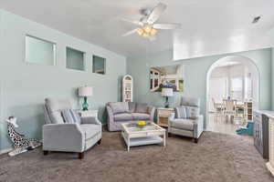 Carpeted living room featuring arched walkways and ceiling fan