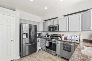 Kitchen featuring stainless steel appliances, dark stone countertops, gray cabinets, light wood-style floors, and recessed lighting