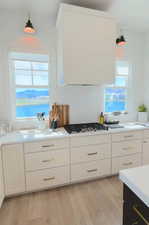 Kitchen featuring white cabinets, ventilation hood, light wood-style floors, stainless steel gas cooktop, and light stone countertops