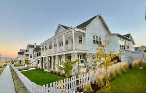 Property exterior at dusk featuring a fenced backyard, stone siding, a balcony, and a residential view