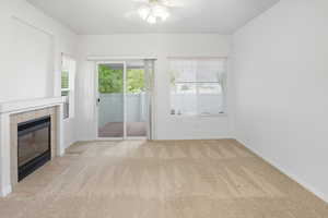 Unfurnished living room featuring light colored carpet, a tiled fireplace, and ceiling fan