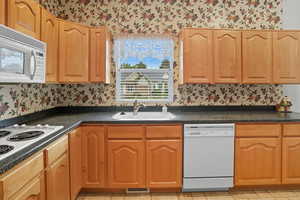 Kitchen with wallpapered walls, white appliances, dark countertops, and light tile patterned flooring