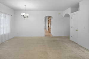 Empty room featuring light colored carpet, a chandelier, and arched walkways