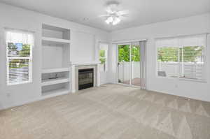 Unfurnished living room featuring built in shelves, healthy amount of natural light, and light colored carpet
