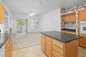 Kitchen featuring dark countertops, white appliances, light colored carpet, a fireplace, and ceiling fan