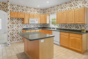 Kitchen with wallpapered walls, a center island, dark countertops, white appliances, and arched walkways