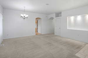 Spare room featuring light carpet, arched walkways, and a chandelier