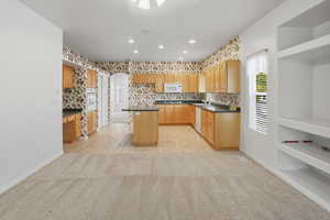 Kitchen featuring dark countertops, decorative backsplash, a center island, light colored carpet, and light tile patterned floors