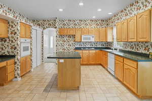 Kitchen with a kitchen island, wallpapered walls, white appliances, recessed lighting, and arched walkways