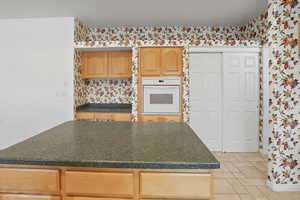 Kitchen featuring oven, a center island, light brown cabinetry, light tile patterned floors, and dark countertops