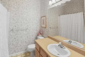 Bathroom with vanity, curtained shower, light floors, and wallpapered walls