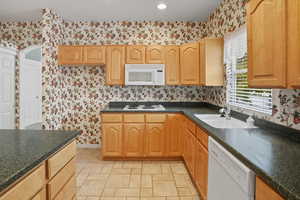 Kitchen with dark countertops, wallpapered walls, white appliances, and recessed lighting