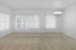 Spare room featuring light colored carpet and a chandelier