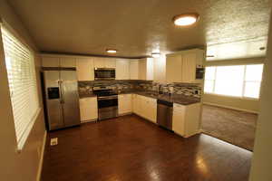 Kitchen with appliances with stainless steel finishes, tasteful backsplash, white cabinets, dark wood finished floors, and a textured ceiling