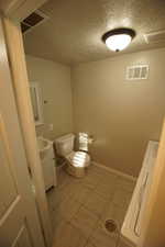 Bathroom with vanity, a textured ceiling, light tile patterned flooring, and washer / dryer