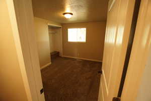 Unfurnished bedroom featuring dark colored carpet, a textured ceiling, and a closet