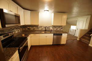 Kitchen with appliances with stainless steel finishes, white cabinets, dark wood-style floors, dark stone counters, and decorative backsplash