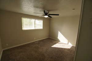 Carpeted empty room with a textured ceiling and ceiling fan