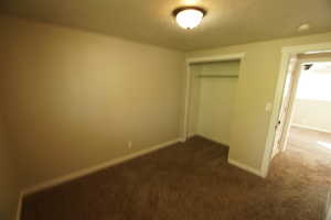 Unfurnished bedroom with dark carpet, a closet, and a textured ceiling