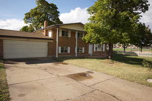 Split level home with brick siding, driveway, an attached garage, and a chimney