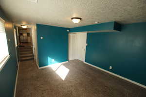 Spare room with carpet flooring, a textured ceiling, and stairs