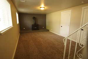 Unfurnished living room featuring dark colored carpet, a textured ceiling, stairs, and a wood stove