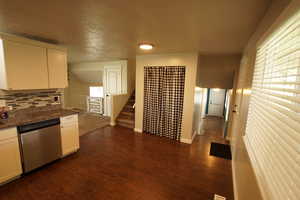 Kitchen with white cabinetry, stainless steel dishwasher, decorative backsplash, dark stone counters, and dark wood-style floors