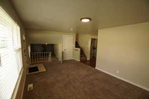 Unfurnished living room featuring stairs, a textured ceiling, and dark colored carpet